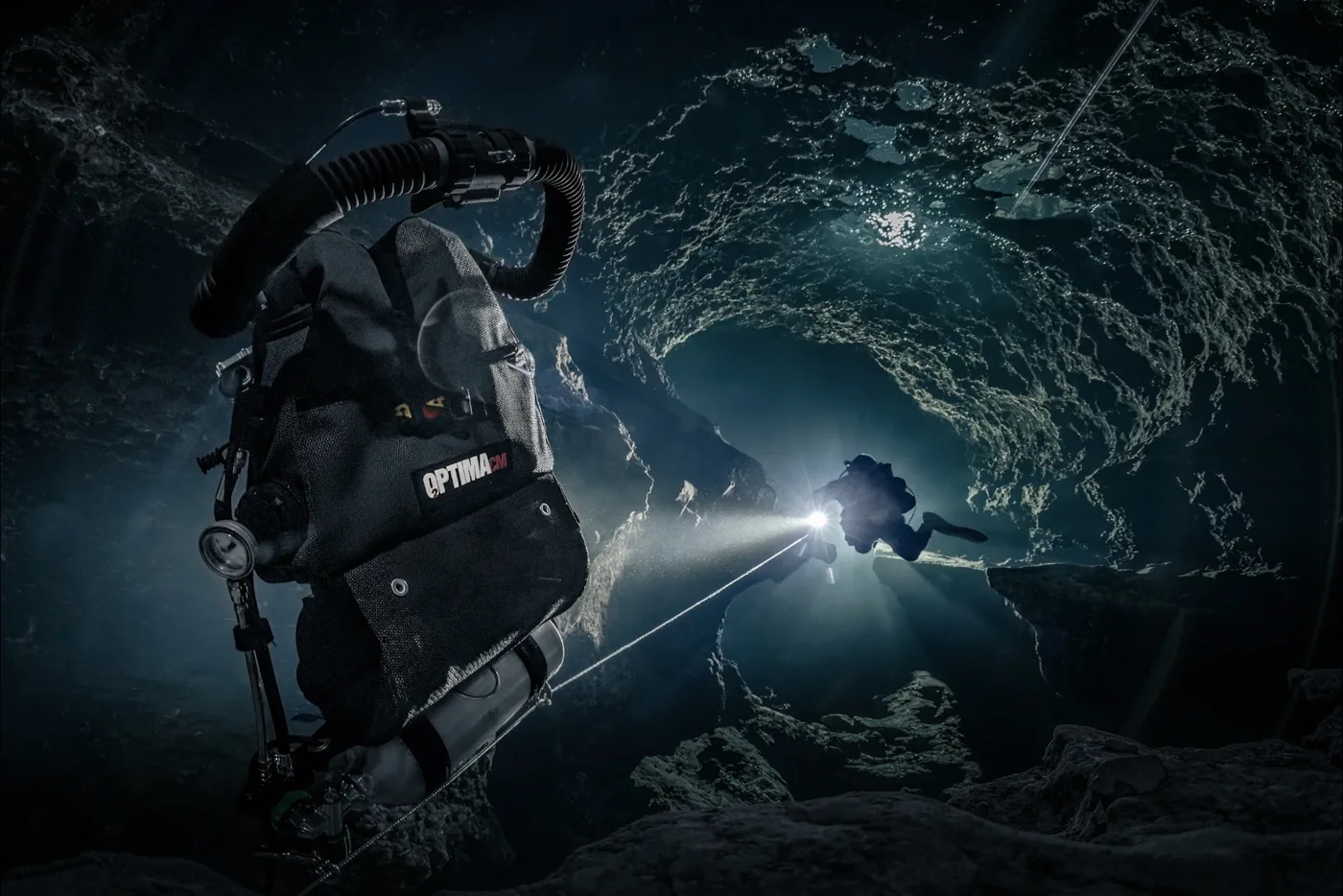Product image of a closed circuit rebreather in a cave, with a diver and light beyond